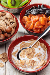  Healthy breakfast. Variety of food on white wooden kitchen table. Cereal flakes with milk, dried fruits and nuts.
