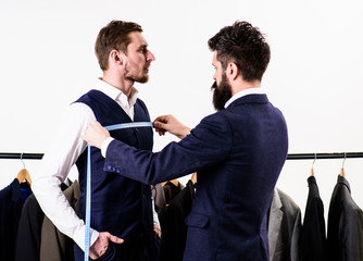 Businessman, client stand near hanger with suits while tailor working.