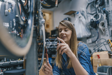 Bike service: mechanic servicewoman repairman installing assembling or adjusting bicycle gear on wheel in workshop