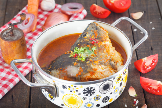 Carp Fish head soup with vegetables in the pot. Tip view. Wooden table filled with ingredients, fresh vegetables, red and black pepper