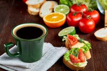 Fresh sandwich with lettuce, tomatoes, cheese on wooden plate, cup of coffee on wooden background, selective focus