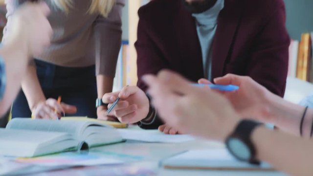 Female team leader standing near table and giving direction to young creative team. Brainstorming of creative group. Colleagues participate in the discussion. Team work in a modern creative agency.