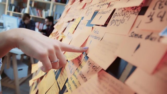 Creative business team brainstorming ideas and concepts. Process of creativity: on black board attach bright paper stickers. Girl points to sticker with ideas, colleagues at work on background