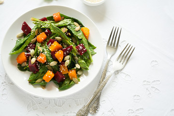 Fresh autumn salad with marinated pumpkin and beetroot, spinach leaves,olive oil, sesame and pumpkin seeds on white table cloth. Space for copy