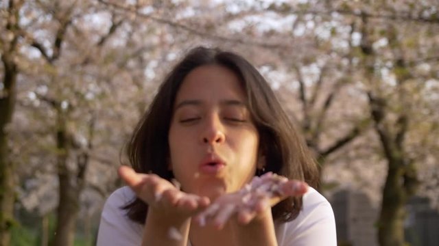 Beautiful Mexican woman blowing sakura leaves from her hands.
