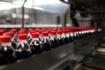 Fototapeta premium Bottling factory - Black juice or soft drink bottling line for processing and bottling juice into bottles. Selective focus.