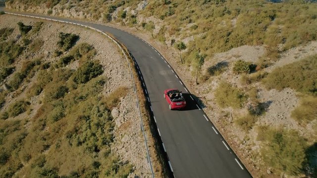 Amazing Epic Inspiring Travel Drone Aerial Shot Following Red Convertible Car With Friends On Empty Mountain Scenic Road Driving Into Sunset, Concept Tourism Destination And Summer Adventures