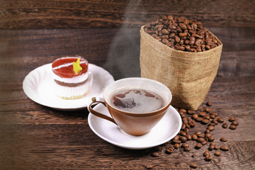 Cup of black coffee and coffee beans in a bag on wooden background with copy space .