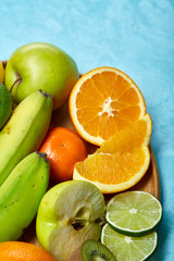 Ripe fresh fruits in a wooden plate on a blue background, selective focus, close-up, top view