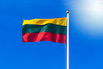 Lithuanian flag waving in the wind against blue sky. Tricolor of yellow, green and red.