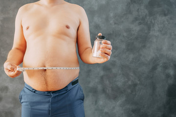 Overweight fat man with measuring tape and slimming pills. Weight loosing, diet, fat burning, pharmacy, medicine concept