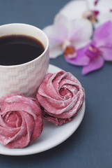 Sweet Pink Meringues and Cup of Coffee on Blue Gray background with Orchid Flowers. Spring Background with copy space. Breakfast.