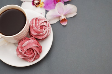 Sweet Pink Meringues and Cup of Coffee on Blue Gray background with Orchid Flowers. Spring Background with copy space. Breakfast.