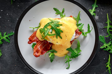 Eggs Benedict on english muffin with crispy bacon, wild rocket salad and hollandaise sauce.