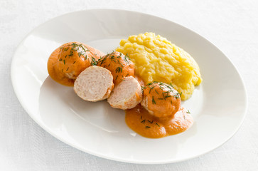 a plate of poultry meatballs with rice under sour cream and vegetables sauce garnished with potato