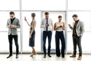 Obraz premium Group of businessmen with phones in their hands standing near the window