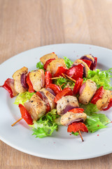 chicken fillet kebabs with roasted peppers, onions and lettuce on wooden skewers are on the plate
