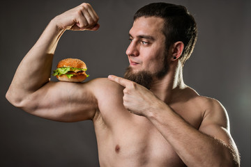 Young man bodybuilder holding burger, unhealthy eating habits.