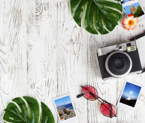 Flatlay with camera, photo, sunglasses, leaves on the white desk.