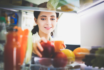 Portrait of female standing near open fridge full of healthy food, vegetables and fruits. Portrait...