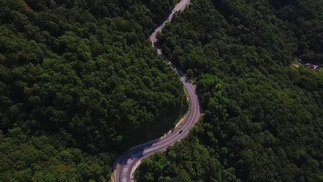 Aerial view flying over old patched two lane forest road with cars van moving green trees of dense woods growing both sides - shot with drone quad copter birds eye view perspective from above.