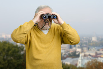 Old man looking through binocular on the city view. Senior tourist observing city locations using binoculars.
