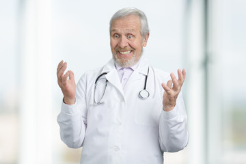 Portrait of amazed old doctor. Senior physician extremely shocked and wondered. Bright blurred background.