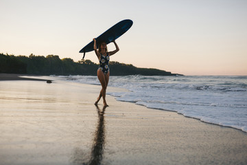 Fototapeta na wymiar sportswoman in swimming suit with blue surfing board walking on beach