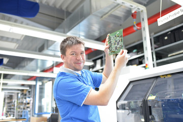 Arbeiter prüft Platine in der Fertigung für Elektronik einer Fabrik // Worker tests motherboard in the production of electronics for a factory