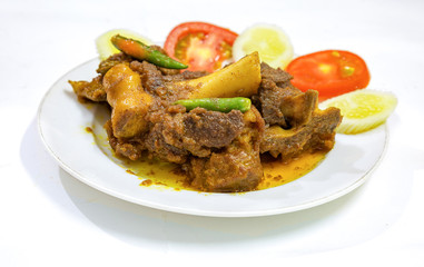 Popular Indian Bengali food meal of spicy mutton curry popularly known as mutton kosha with green chili and sliced tomato and cucumber.