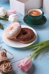 donuts, coffee and tulips on a blue wooden background.