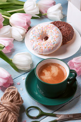 donuts, coffee and tulips on a blue wooden background.