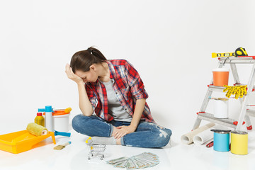 Upset sad woman holds bundle of cash money, supermarket grocery push cart for shopping. Instruments for renovation apartment isolated on white background. Wallpaper accessories. Concept of repair home