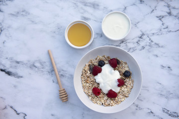 Obraz na płótnie Canvas White bowl of muesli with raspberries, blueberries and a pot of honey and yogurt 