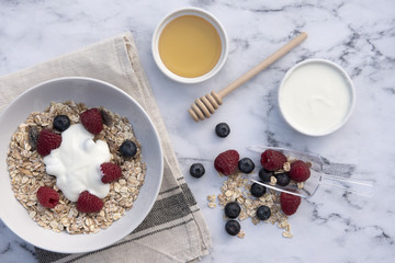 White bowl of muesli with raspberries, blueberries and a pot of honey and yogurt 