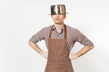 Fun man in striped apron with silver stainless glossy aluminium empty stewpan, pan or pot on head isolated on white background. Male housekeeper or houseworker. Kitchenware, dishes, cuisine concept.