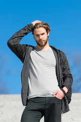 Fototapeta premium Mens fashion and style. Man with beard in casual wear touch hair on sunny outdoor, fashion. Macho stand on blue sky, perspective. Perspective, future, freedom.