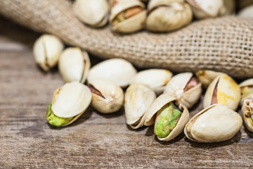 pistachio nuts on wooden table with pistachio in gunny sack background, close up shot