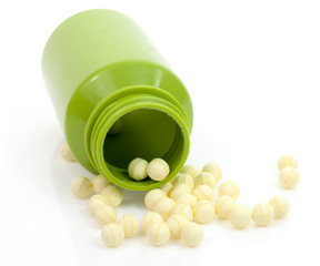 Round yellow probiotic tablets spilling from green medication bottle against white background.