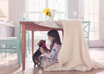 Young girl crouching under a table with her small dog
