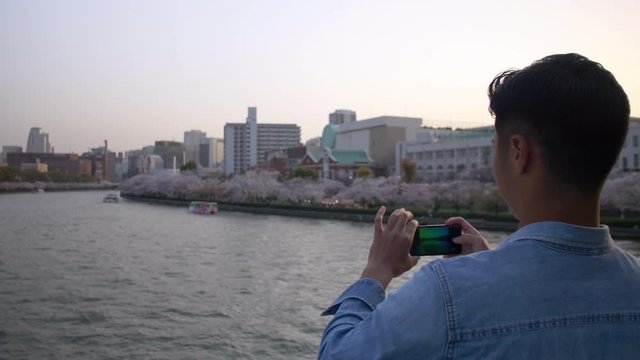 Handsome man taking photos of beautiful sakura from a bridge.