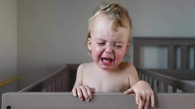 Crying baby in crib at home close up