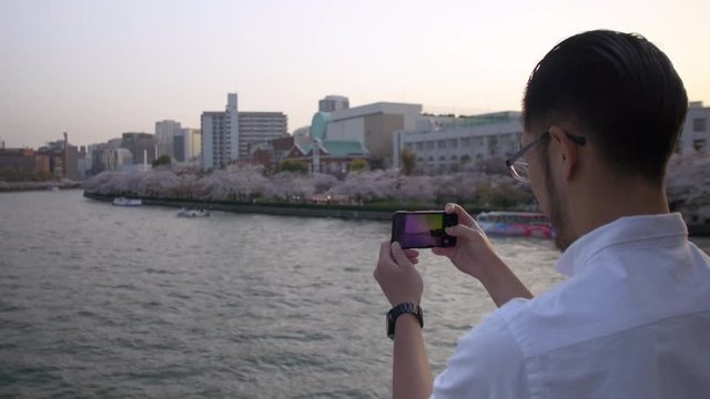 Handsome man taking photos of beautiful sakura from a bridge.