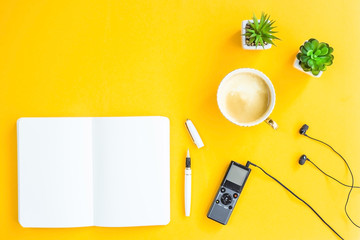 Workplace of the journalist with a dictaphone, headphones, a notebook, a pen and green plants on a yellow background. Flat lay, top view. Copyspace