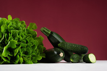 Green summer vegetables on white wood board and bordo kitchen wall. Modern elegant colorful concept kitchen interior.