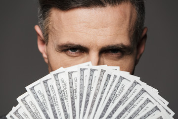 Extreme closup photo of confident man 30s holding fan of money dollar bills at face and looking on...