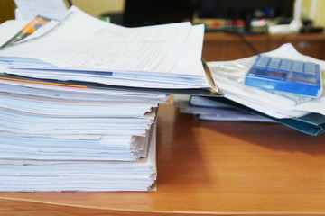 Paperwork at the office. Pile of documents on wooden table, side view. Paper sheets in cardboard folders stacked on the desk. Business and finance concept