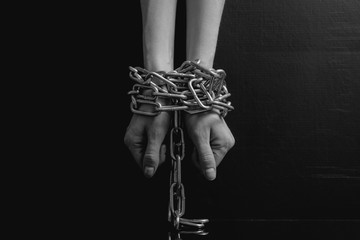 Black and white minimalistic image. women's hands chained close-up on a black background, toned to...