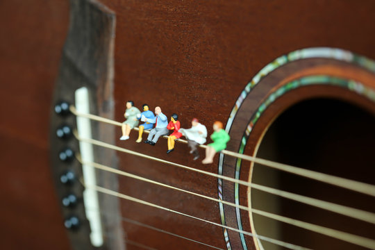 Miniature people: Businessman reading newspaper and sitting on acoustic guitar,time of relax or music relax,stationary,business concept.