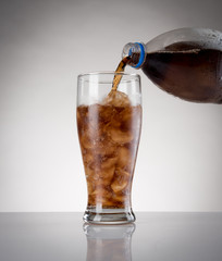 Pour cola from bottle to glass with ice on the gray background